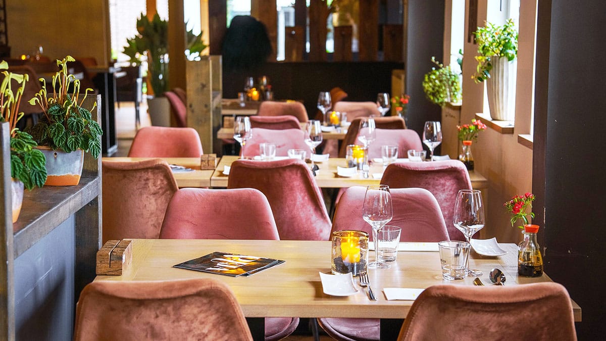 Restauranttafels met roze fluwelen stoelen en kaarslicht
