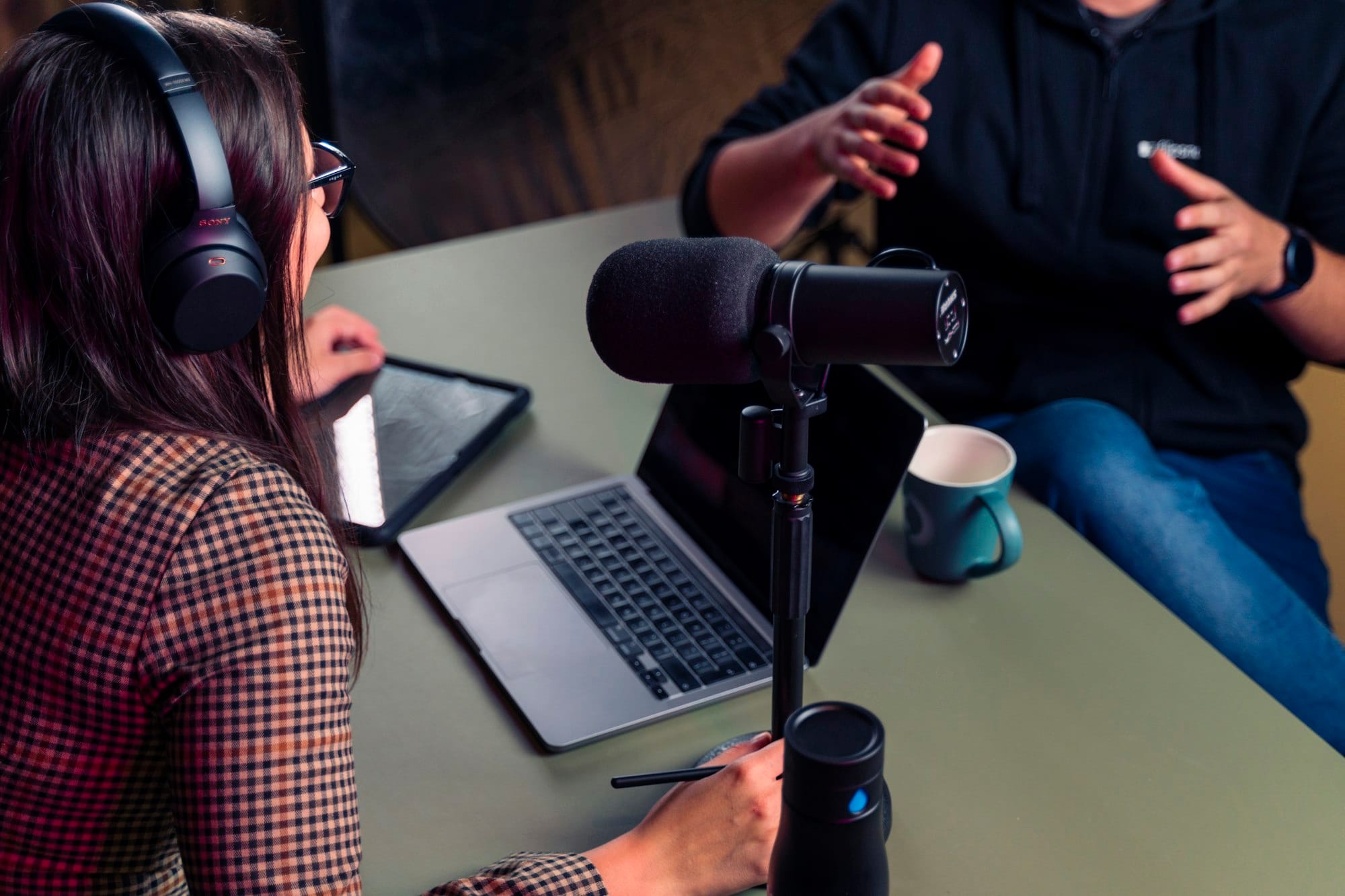 Podcastgesprek aan tafel met microfoon, laptop en koptelefoon