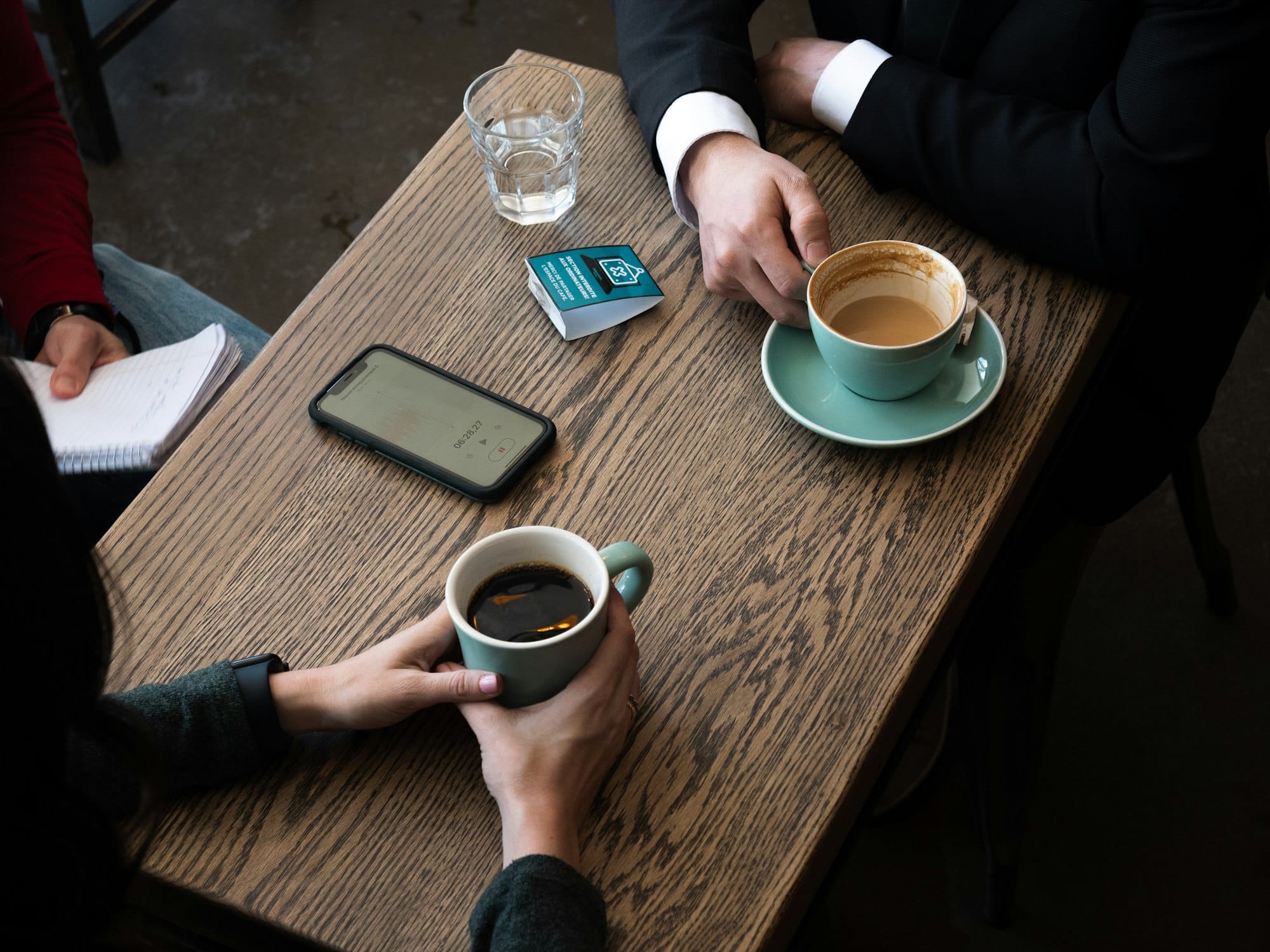 Twee mensen met koffie en een notitieboek aan een houten tafel